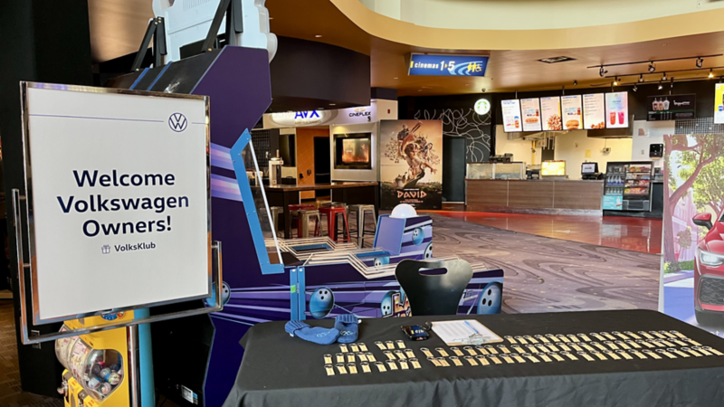 A collage featuring a dad with three kids holding branded cards, a family posing in a VW cutout, and the welcome table. 