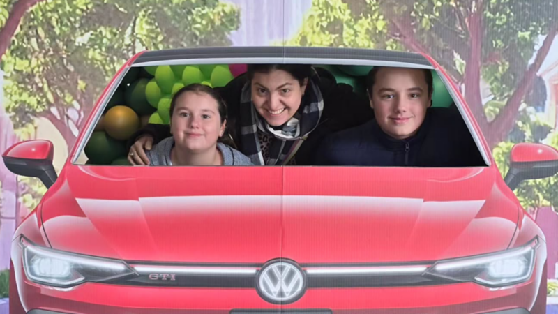 A collage featuring a dad with three kids holding branded cards, a family posing in a VW cutout, and the welcome table. 
