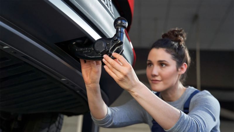Een monteur monteert een afneembare trekhaak onder de bumper van een auto.