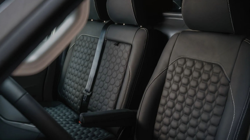 Interieur van een bedrijfswagen met zwarte lederen voorstoelen, een honingraatpatroon op de zitting en rugleuning, en witte stiksels.