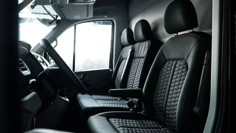 Interieur van een bedrijfswagen met zwart lederen stoelen voorzien van een gestikt honingraatpatroon en rode accenten.