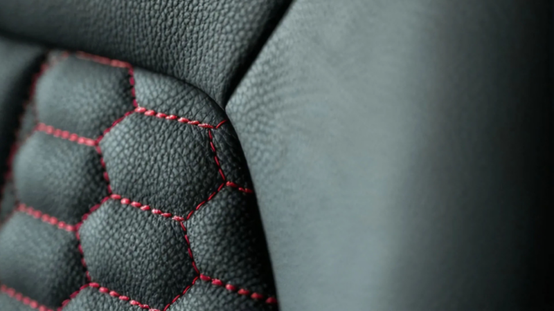 Detailopname van zwart generfd leer met rode stiksels in een honingraatpatroon.