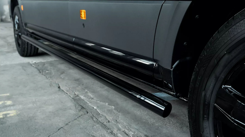 Glanzend zwarte ronde side-bar gemonteerd onder de dorpel van een matzwarte Volkswagen Crafter.