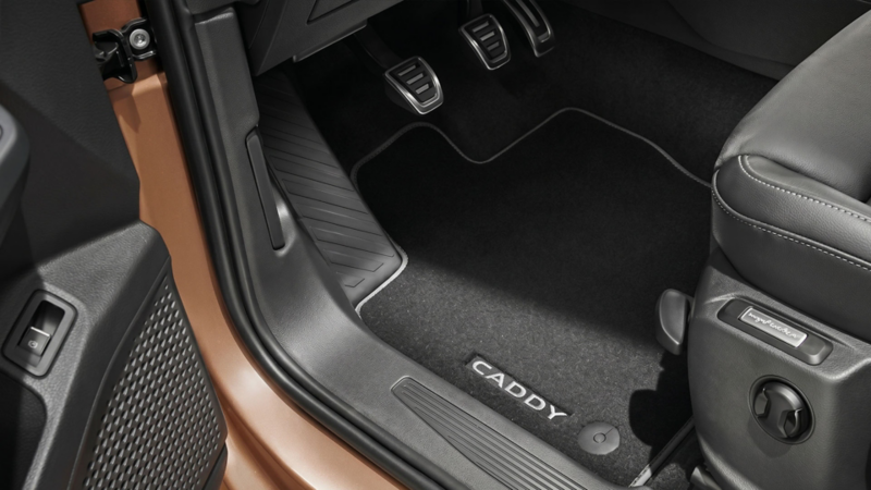 Zwarte velours vloermat met witte Caddy-opdruk en grijze bies in de voetenruimte van een Volkswagen Caddy.