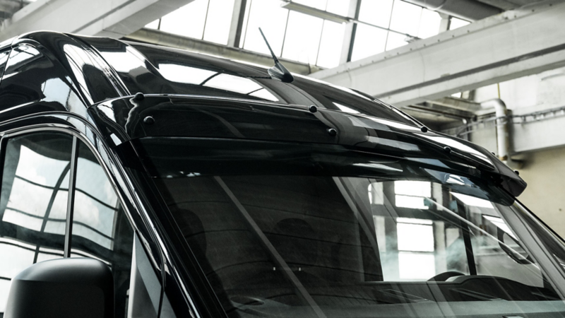 Donker getinte externe zonneklep gemonteerd boven de voorruit van een zwarte Volkswagen Crafter.