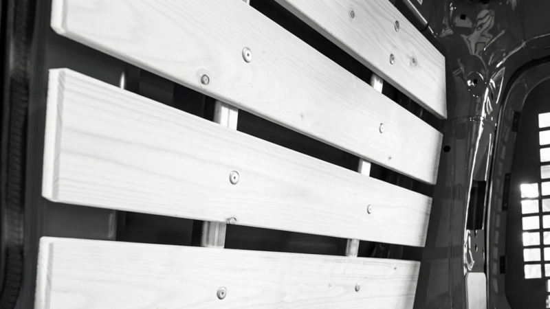 Horizontale houten latbekleding voor wandbescherming in de laadruimte van een Volkswagen bedrijfswagen.
