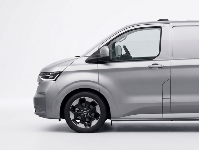 Zilverkleurige Volkswagen Transporter eHybrid waarvan de batterij wordt opgeladen via een aangesloten laadkabel.