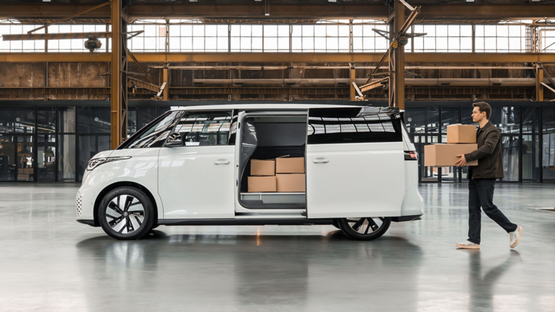 Een man draagt dozen naar de geopende schuifdeur van een witte Volkswagen ID. Buzz toCargo in een industriële hal.