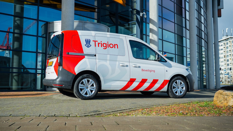 Zij- en achteraanzicht van een witte Volkswagen Caddy Kombi eHybrid toCargo met Trigion Beveiliging logo en rode bestickering.