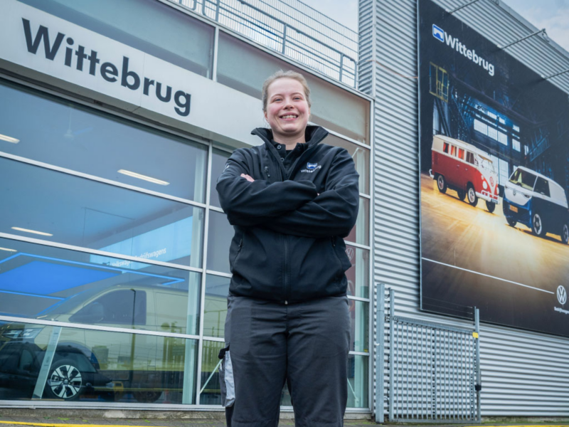 Een glimlachende autotechnicus van Wittebrug staat met overmekaar geslagen armen voor de showroom.