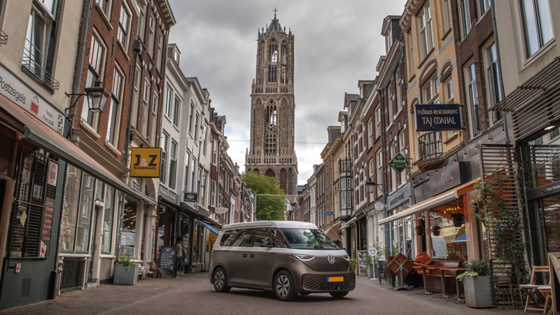 De ID. Buzz camper van Outbase geparkeerd in het centrum van Utrecht met op de achtergrond de Domtoren