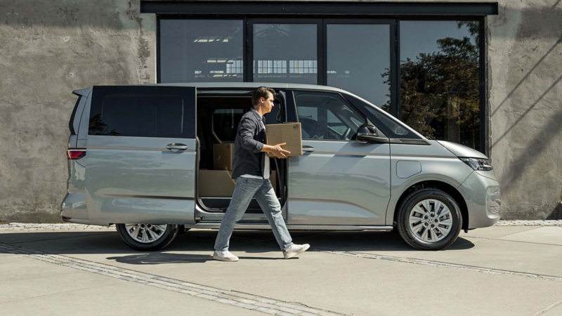Zijaanzicht van de Multivan eHybrid met Cargo Accessoire Pakket met geopende zijdeur en man die dozen aan het inladen is