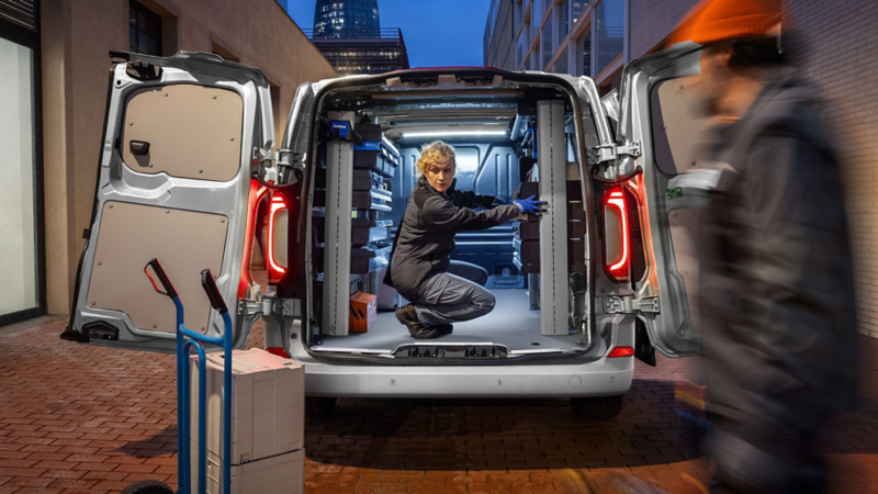 Nieuwe Transporter met beide achterdeuren geopend en een vrouw die gehurkt in de laadruimte zit 
