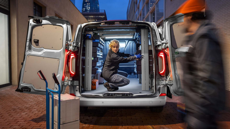 De nieuwe Volkswagen Transporter met geopende achterdeuren en een vrouw die gehurkt zit in het laadruim
