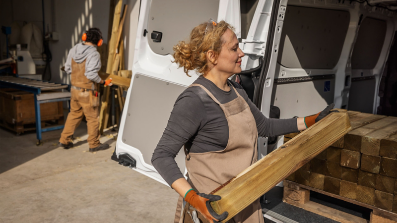 Vrouw die houten balk in het laadruim van de nieuwe e-Transporter aan het laden is