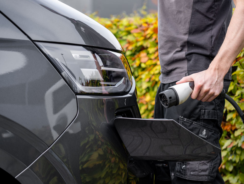 Een man sluit een laadkabel aan op het oplaadpunt van een grijze Volkswagen bedrijfswagen.