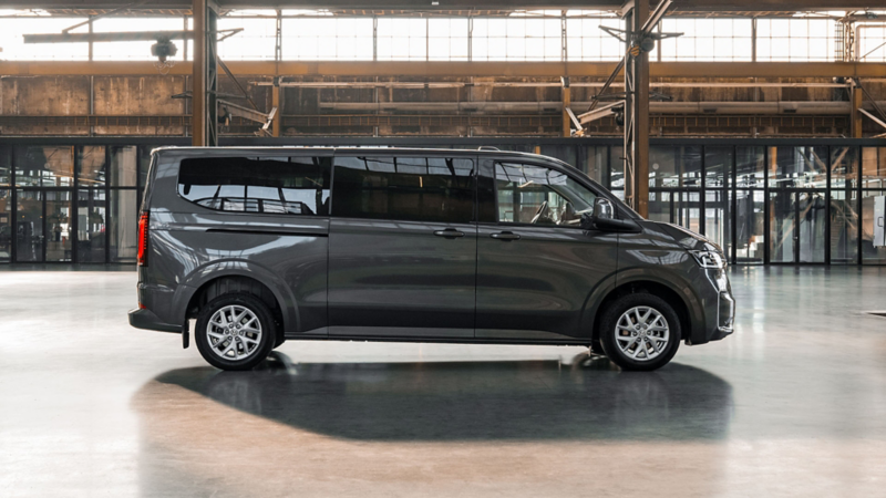 Zijaanzicht van een grijze Volkswagen Transporter Kombi eHybrid toCargo in een grote industriële hal.