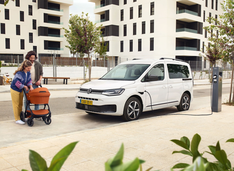 Caddy Kombi eHybrid aangesloten op een laadpaal met een gezin en een kinderwagen