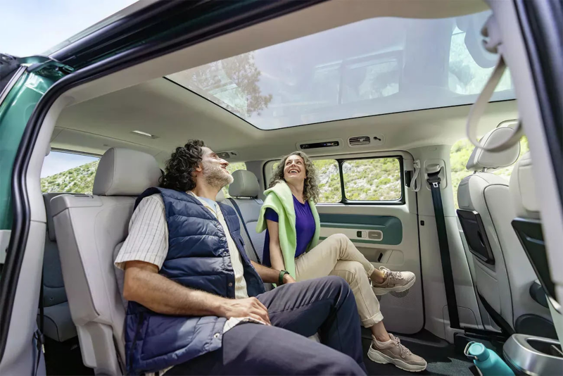 Twee mensen die op de achterbank van de ID. Buzz zitten en naar het panoramadak aan het kijken zijn