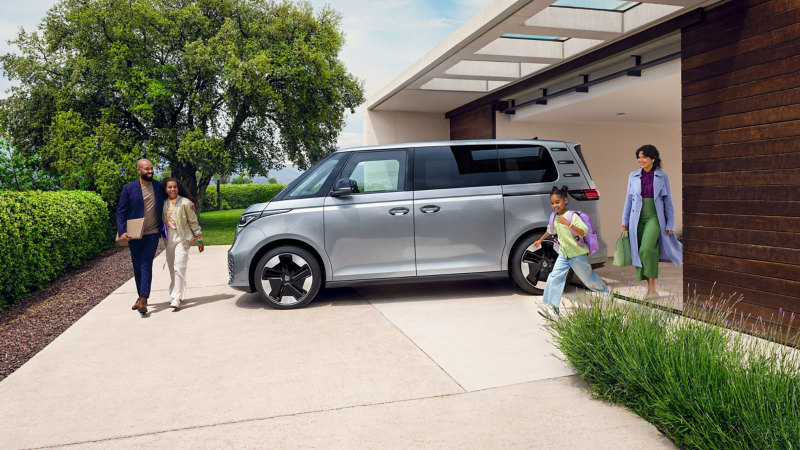 ID. Buzz geparkeerd op de oprit van een luxe villa met een gezin eromheen