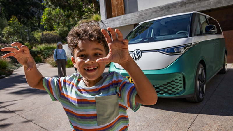 Detailbeeld van een vrolijk kind met op de achtergrond de ID. Buzz die op de oprit geparkeerd staat