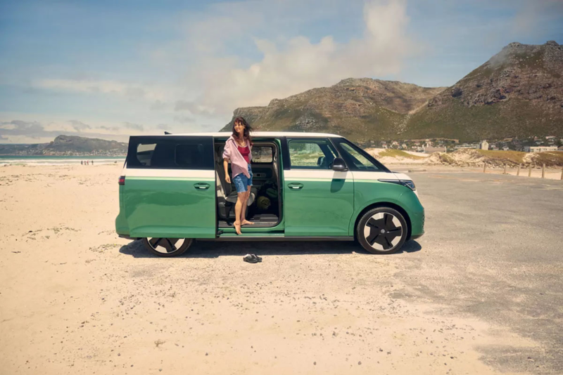 ID. Buzz op het strand met een vrouw die in de deuropening staat
