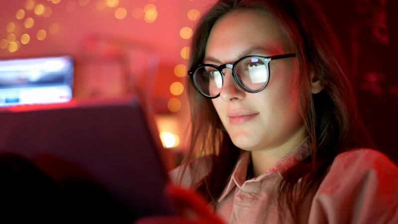 Eine junge Frau mit Brille schaut auf ihr Tablet