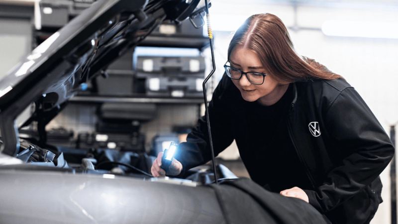 a woman inspecting under the hood of a VW car