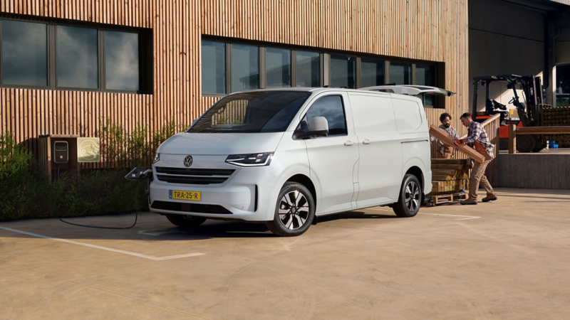 Nieuwe Transporter eHybrid aan het opladen bij een laadpaal met daarachter twee mensen die spullen aan het inladen zijn