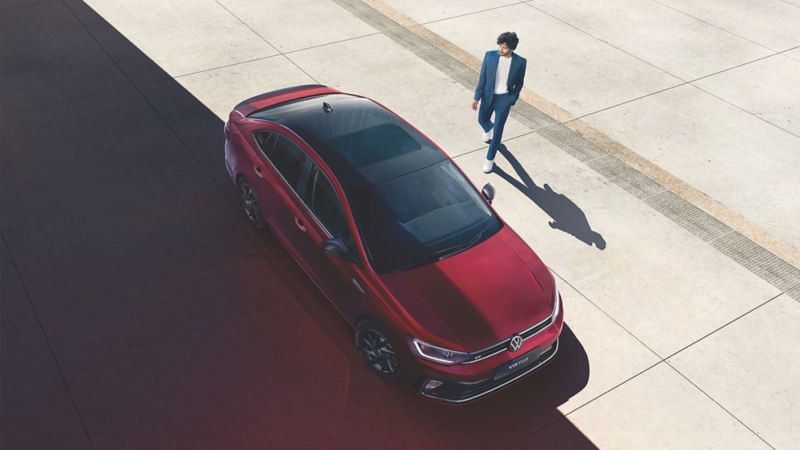 Nuevo Virtus de Volkswagen en color rojo con techo negro. Joven se acerca para abrirlo.