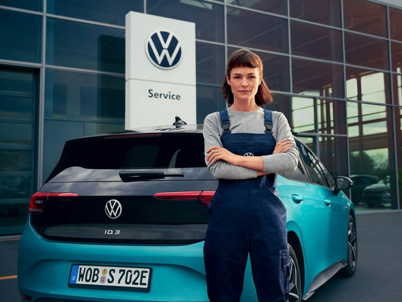 Volkswagen monteur staat achter een ID3 buiten een showroom en kijkt naar de camera