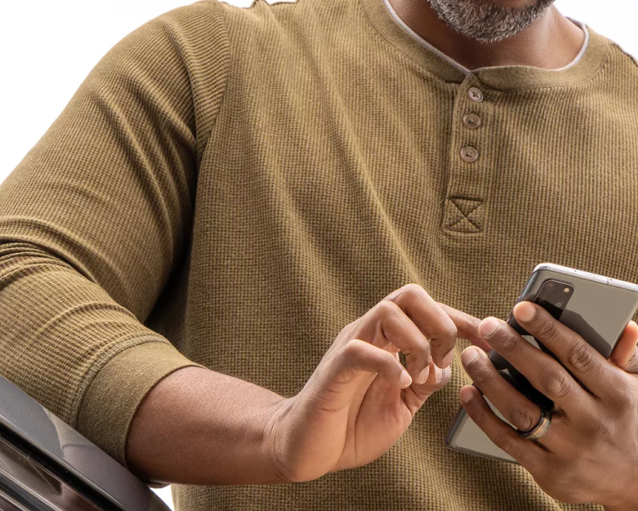 Las manos de un hombre con una camiseta polo VW verde oliva sostienen un teléfono inteligente.