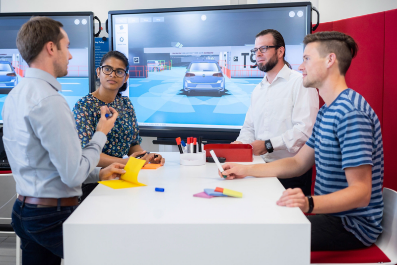 A team of Volkswagen employees stands around a table and consults in front of monitors with traffic simulations