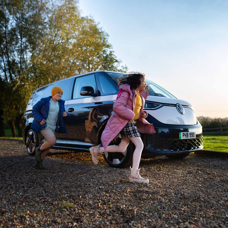 Family running past parked Volkswagen ID. Buzz outdoors