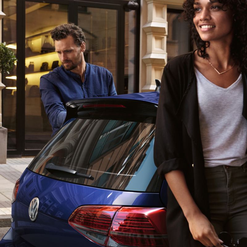 Un homme et une femme debout à côté d'une Golf, examinant le manuel du propriétaire VW.