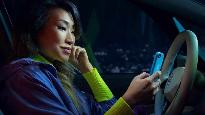 Vrouw achter stuur in stilstaande auto met telefoon in de hand