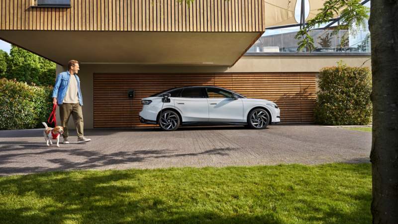 Ein grauer ID.7 ist an einer ID. Charger 2 angeschlossen, davor ein Mann mit einem Hund