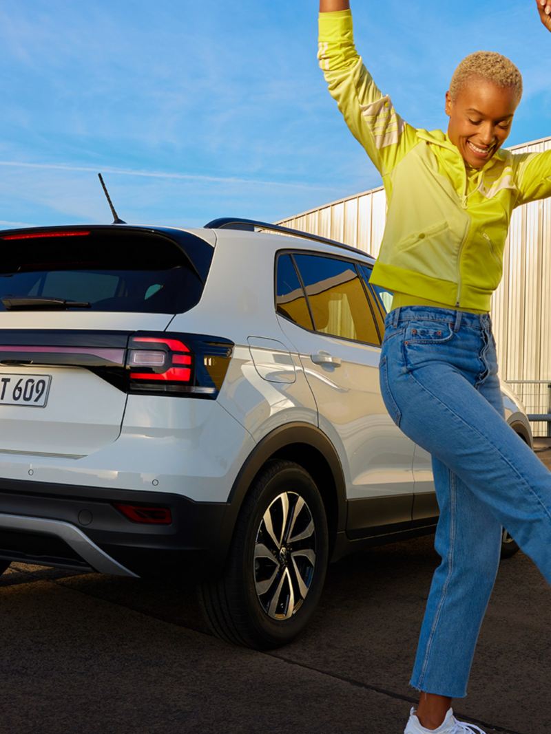 Eine Frau tanzt vor einem weißen VW T-Cross ACTIVE.