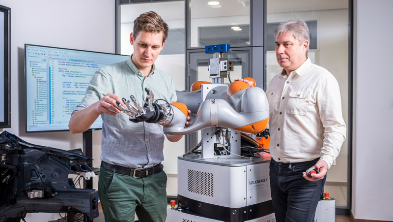 Two VW employees work on a robotic hand