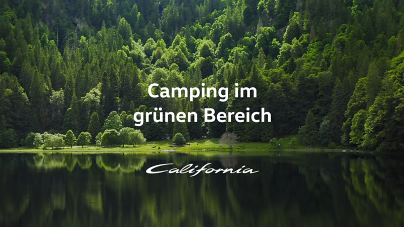 Schriftzug "Camping im grünen Bereich" auf einem ruhigen See umgeben von hohen Tannen.