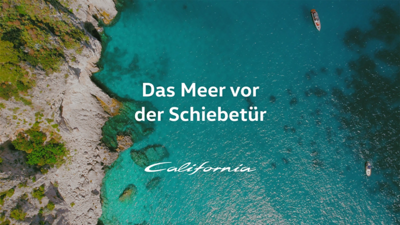 Draufsicht auf türkisblaues Meer mit Booten und felsiger Küste am Bildrand.