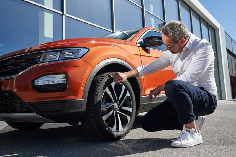 Un collaboratore Service tocca lo pneumatico di un'auto Volkswagen per verificare la presenza di danni.