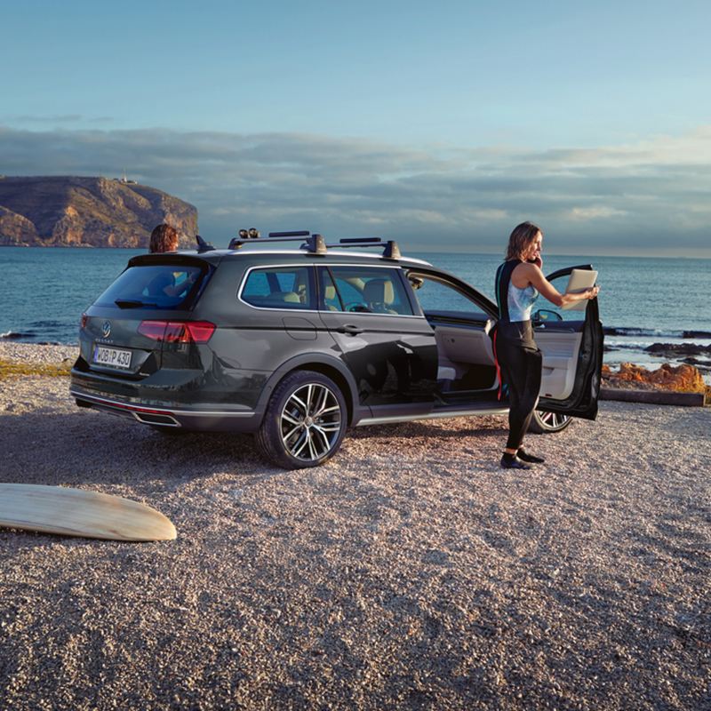 donna apre porta anteriore passeggero di Nuova Passat Alltrack VW parcheggiata in spiaggia