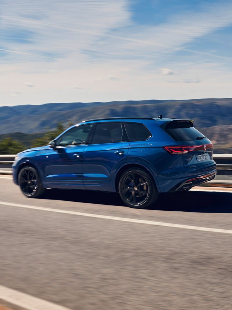Blue Touareg R PHEV SUV driving in the sun along open road