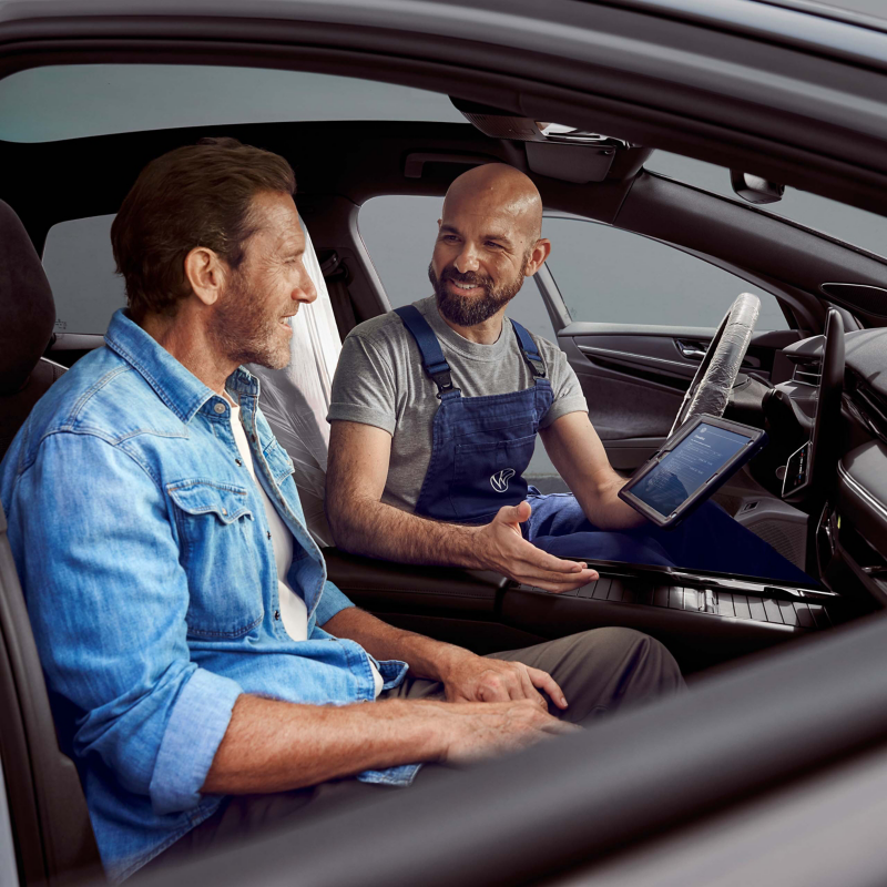 Kunde sitzt im Auto, VW Servicemitarbeiter erklärt ihm etwas auf dem Tablet.