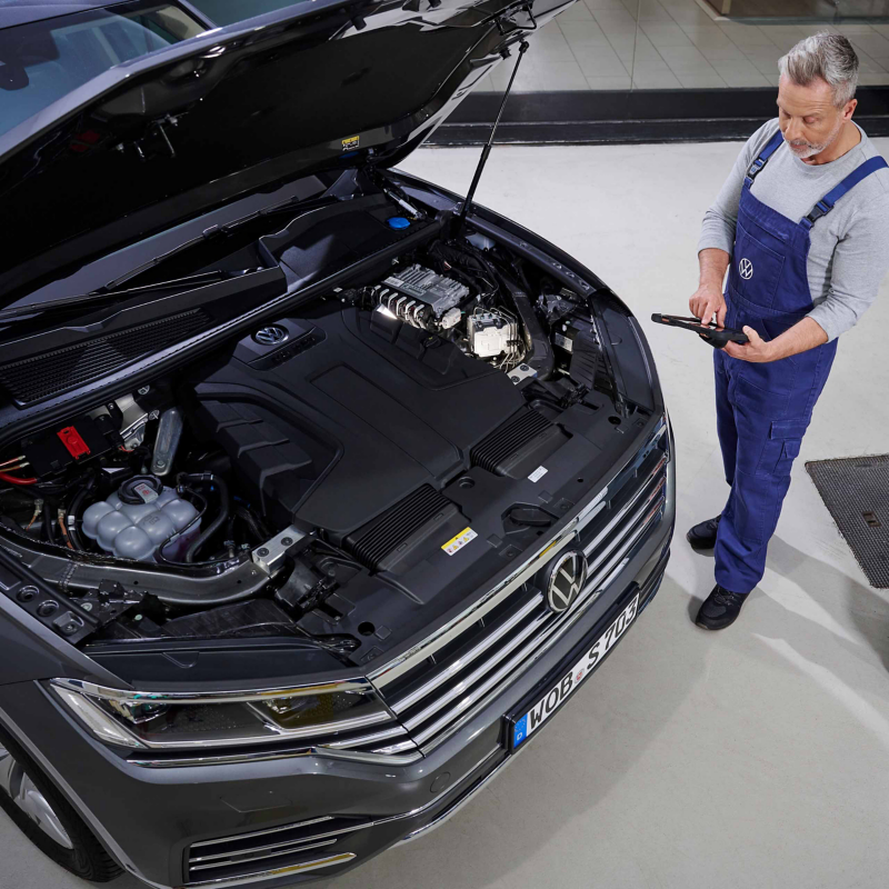 Τεχνικός service VW ελέγχει τον χώρο του κινητήρα ενός VW με Ανταλλακτικά Ανταλλαγής Volkswagen.
