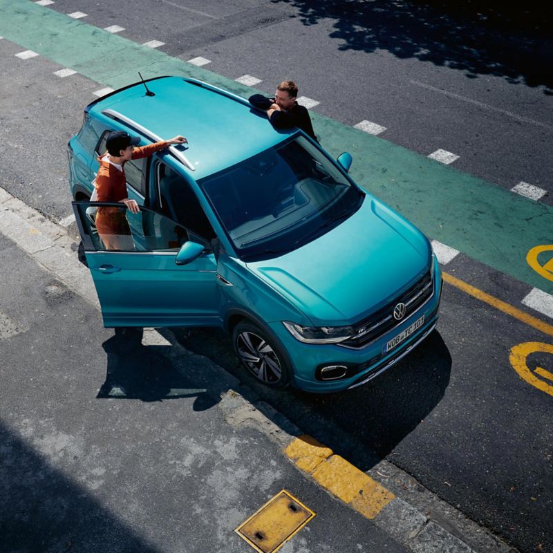 Mann und Frau stehen an geöffneten Türen des VW T-Cross Front, türkises Fahrzeug auf Straße