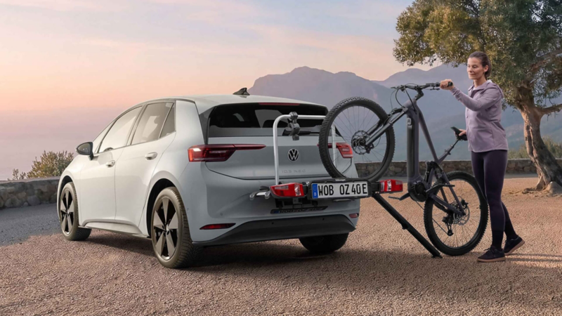 Mujer utilizando una rampa para bicicletas para subir una bicicleta eléctrica a un portabicicletas de Volkswagen Accesorios instalado en un VW ID.3 Neo.