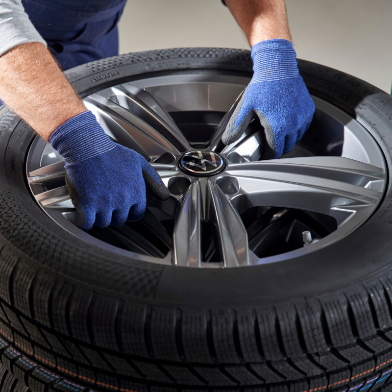  Gros plan des mains gantées de bleu d'un mécanicien installant une roue en alliage Volkswagen sur un pneu.