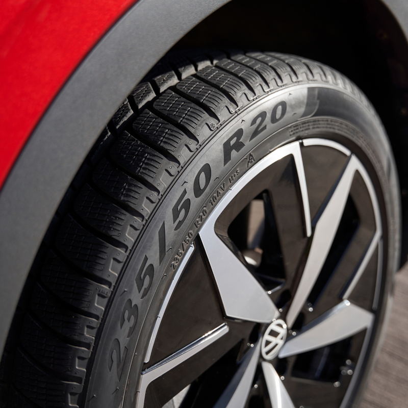 Vue rapprochée d'un pneu et d'une roue de voiture, le pneu affichant clairement "235/50 R20" et la roue présentant un design multibranches noir et argent avec le logo Volkswagen au centre.